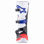Botas Alpinestars Tech 3, botas de motocross, brancas, vermelho vivo e azul escuro, vista frontal apresentando a placa de canela protetora em TPU com logótipo azul, sistema de fecho de tripla fivela e biqueira vermelha reforçada