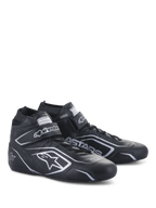 Sapatos Alpinestars Tech-1 T V3 FIA, sapatos de automobilismo, pretos e prateados, construção em couro bovino com logótipos e branding Alpinestars prateados, vista lateral angulada com tira de gancho e laço e fecho de cadarços