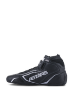 Sapatos Alpinestars Tech-1 T V3 FIA, sapatos de automobilismo, pretos e prateados, vista de perfil lateral, construção integral em couro bovino com logótipo ASTARS prateado, tira ajustável de gancho e laço e gola elástica à prova de fogo.