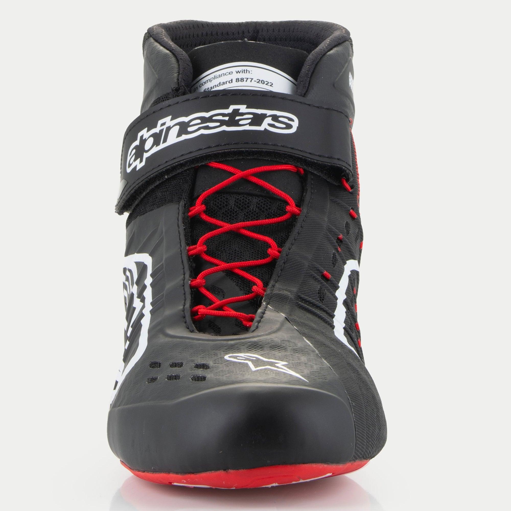 Sapatos Alpinestars Tech-1 KX V3, sapatos de karting, pretos, brancos e vermelhos, vista frontal com atacadores assimétricos vermelhos, tira de velcro preta no tornozelo com logótipo branco e etiqueta de certificação FIA 8877-2022 visível na língua.