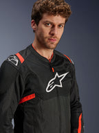 Casaco Alpinestars T-Sps Air V2, preto com detalhes em vermelho fluo, casaco de motociclismo em malha têxtil, vestido por modelo, com o logótipo Alpinestars branco no peito e ombros, painéis de malha respirável, estilo de condução urbana desportivo