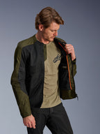 Casaco Alpinestars C-1 Air em caqui e preto, modelo masculino a mostrar o forro interior laranja e o compartimento impermeável, painéis de malha técnica para fluxo de ar, estilo urbano contemporâneo com t-shirt verde azeitona e calças pretas