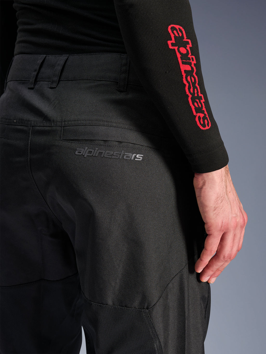 Alpinestars C-1 Air Pants, calças de motociclismo em tecido preto, vista aproximada do bolso traseiro com logótipo Alpinestars cinzento subtil, painéis de malha respirável e polifibra durável, concebidas para conforto na condução urbana