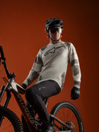 A-Dura Ride Long Sleeve Jersey in Sand Camo with Alpinestars chest logo, worn by an MTB rider on a mountain bike.