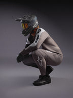 Camisola de BTT A-Supra Elite cinzento desbotado e calças a condizer, com capacete integral preto e óculos de corrida.