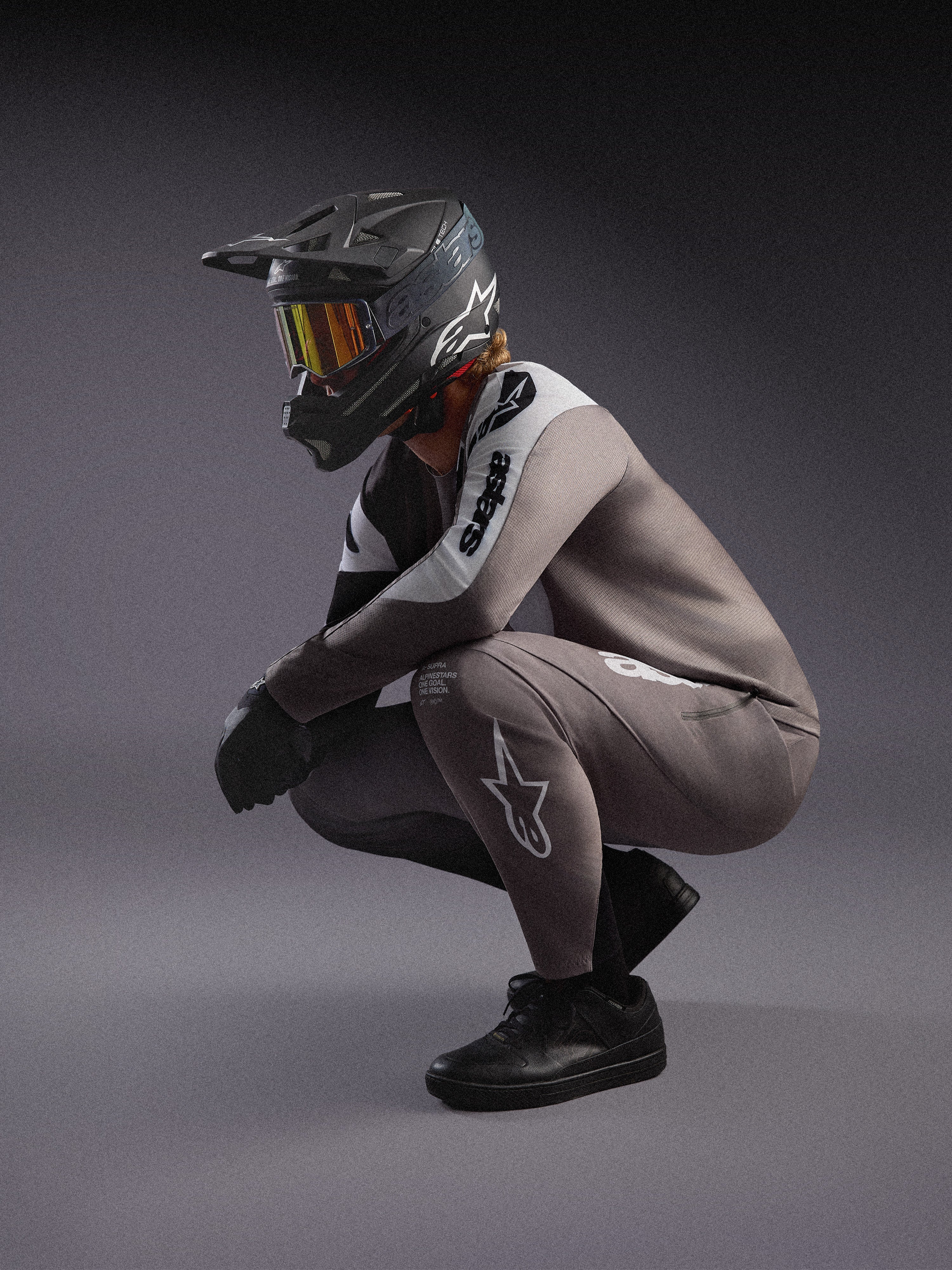 Camisola de BTT A-Supra Elite cinzento desbotado e calças a condizer, com capacete integral preto e óculos de corrida.