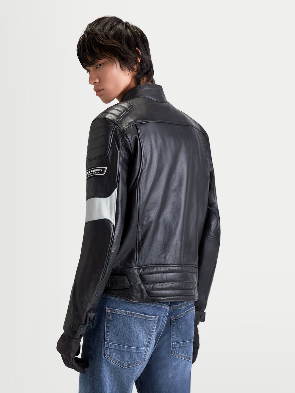 Alpinestars Revern casaco de couro, casaco de moto urbano para homem em preto e cinzento metalizado, vista traseira num modelo a usar calças de ganga, exibindo construção em couro envelhecido e estilo heritage