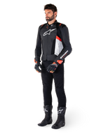 Alpinestars Missile V3 Airflow Leather Jacket, Black White Red Fluo, worn by a male model with black pants, black racing gloves, and black boots, featuring perforated leather for ventilation, a white chest logo, and red fluo accents, designed for premium racing and sport performance.