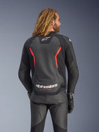 Casaco de Pele Alpinestars GP Force V2, Preto e Vermelho Fluo, vista traseira num modelo, com o logótipo Alpinestars branco e o texto 'RACING AHEAD', combinado com calças e luvas de motociclismo em pele preta.