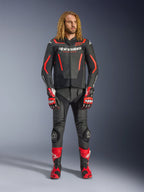Modelo masculino a usar o casaco de pele Alpinestars GP Force V2 em preto e vermelho flúor, combinado com calças de pele a condizer, luvas de corrida vermelhas e botas de performance vermelhas, equipamento desportivo profissional para motociclismo