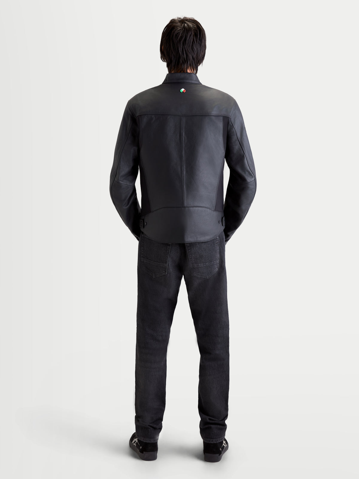 Alpinestars Maver X casaco de couro, casaco de moto urbano contemporâneo para homem, preto, vista traseira num modelo com calças de ganga e sapatos escuros, a mostrar construção em pele premium e pormenor da gola