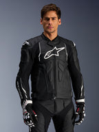 Alpinestars Dusk Leather Jacket, preto e branco, casaco de motociclismo em pele com áreas de proteção acolchoadas e logótipos brancos, usado com luvas de corrida pretas e brancas com detalhes em vermelho, equipamento de condução desportiva profissional