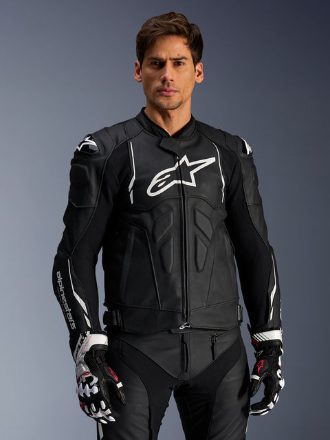 Alpinestars Dusk Leather Jacket, preto e branco, casaco de motociclismo em pele com áreas de proteção acolchoadas e logótipos brancos, usado com luvas de corrida pretas e brancas com detalhes em vermelho, equipamento de condução desportiva profissional