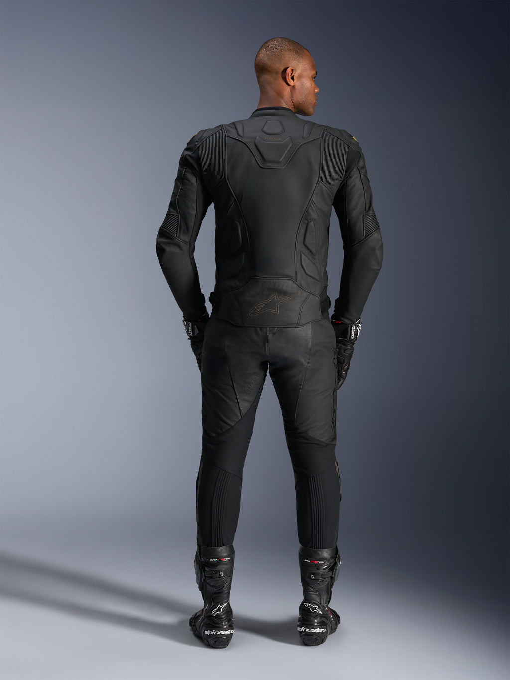 Alpinestars Dusk Leather Jacket, Black Laser, rear view on a rider, worn with matching leather motorcycle pants, racing gloves, and boots, featuring ergonomic 3D multi-panel construction and protective leather panels.