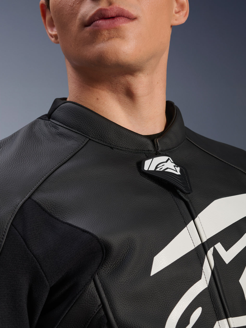 Blusão de Couro Alpinestars GP Plus V4, blusão de motociclismo desportivo, preto e branco, grande plano da gola em couro texturizado e da aba com o logótipo Alpinestars, gráfico branco no peito, design derivado da competição