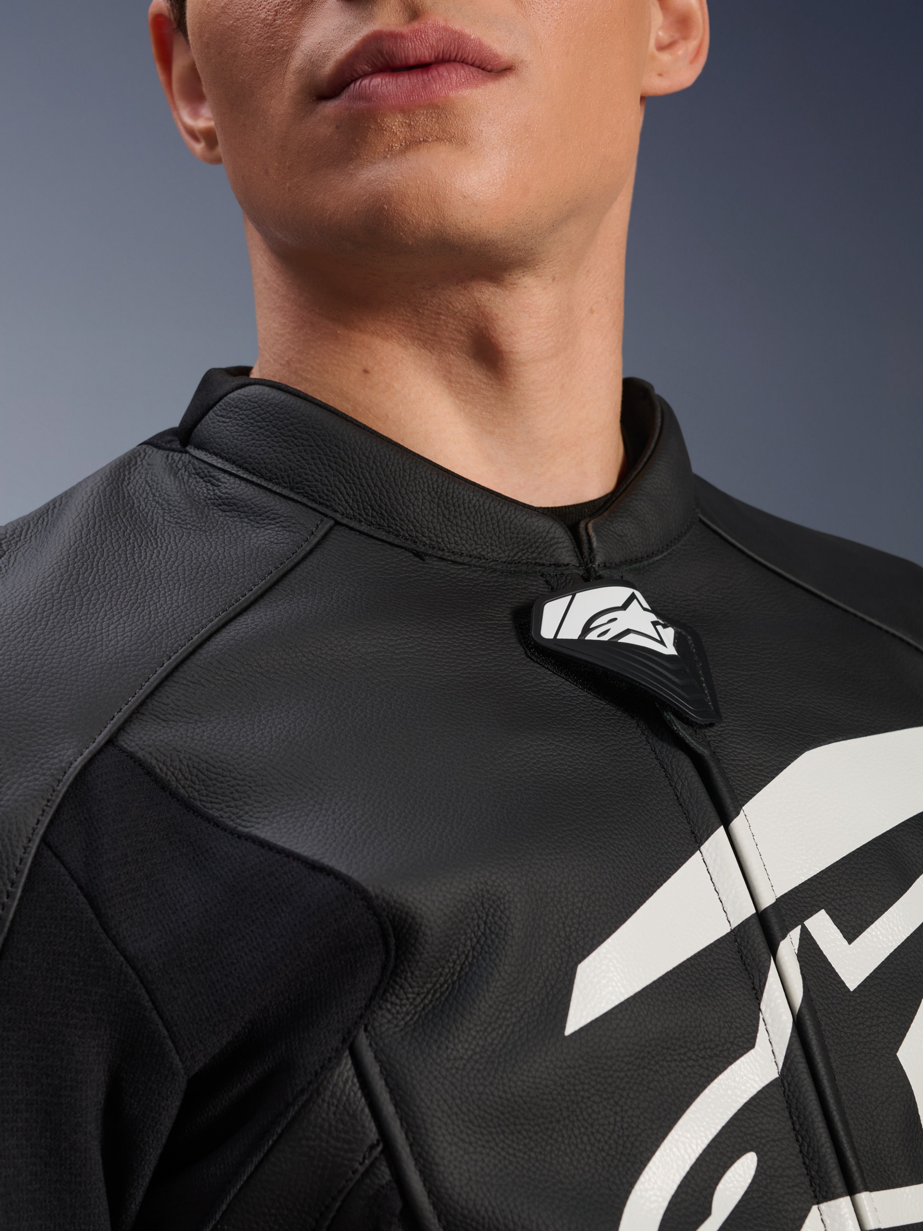 Blusão de Couro Alpinestars GP Plus V4, blusão de motociclismo desportivo, preto e branco, grande plano da gola em couro texturizado e da aba com o logótipo Alpinestars, gráfico branco no peito, design derivado da competição