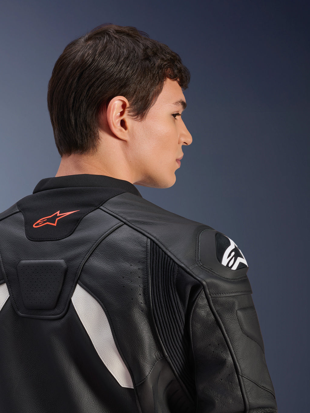 Casaco de Couro Alpinestars GP Plus V4, preto e branco, vista traseira em grande plano de um modelo a usar o casaco, com um logótipo vermelho na gola, protetores de ombros brancos e construção em couro durável com painéis elásticos