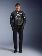 Modelo masculino a usar o Casaco de Couro Alpinestars GP Plus V4, preto e branco, com logótipo Astars em branco no peito e detalhes brancos nos ombros, combinado com luvas e calças pretas, vestuário de motociclismo de estilo desportivo