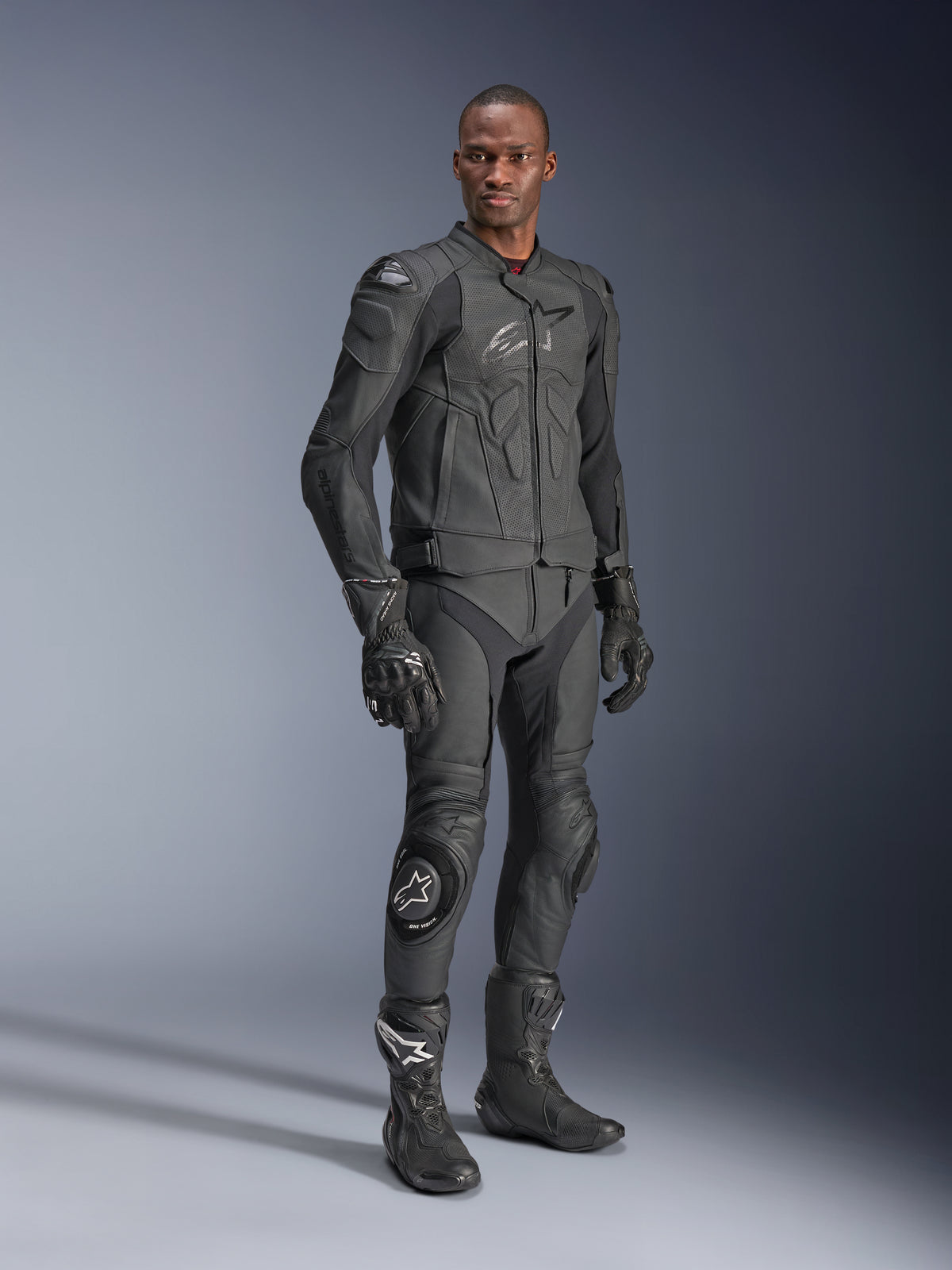 Casaco de Couro Alpinestars Dusk Airflow, Preto, usado por um piloto com equipamento técnico completo, incluindo calças de couro a condizer, luvas e botas, com painéis de couro perfurado para ventilação e armadura integrada para condução desportiva de motociclos