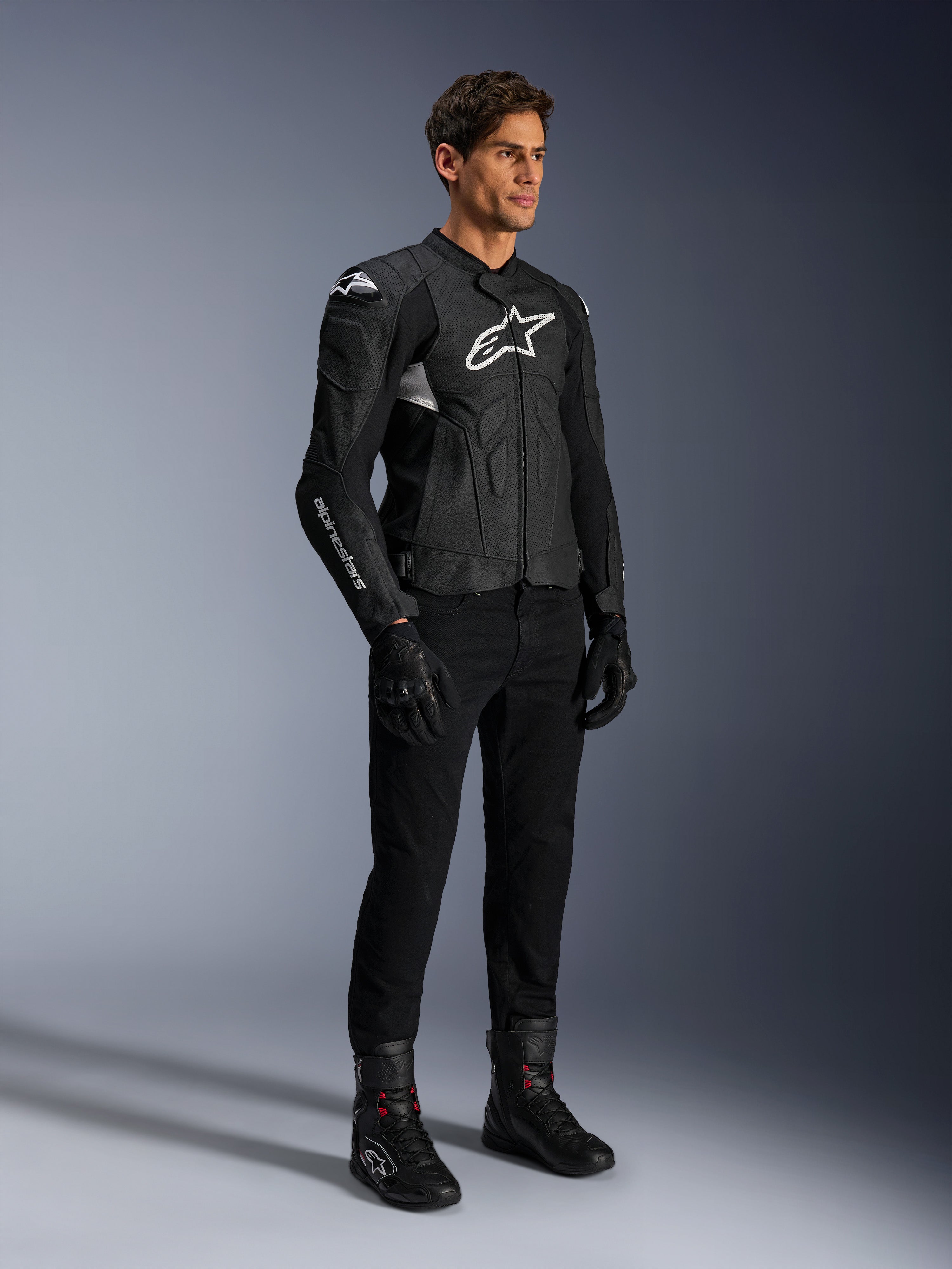 Casaco de Couro Alpinestars Dusk Airflow, preto e branco, combinado com calças de motociclismo, luvas e botas pretas, apresentando painéis de couro perfurado, logótipos brancos e estilo desportivo de estrada