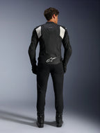 Casaco de Couro Alpinestars Dusk Airflow, Preto e Branco, vista traseira de um piloto a usar calças e botas pretas, com couro perfurado para ventilação, painéis de acordeão brancos nos ombros e logótipo branco na parte inferior das costas