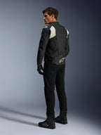 Alpinestars Dusk Airflow Leather Jacket, Preto e Branco, vista traseira de modelo a usar o casaco de couro perfurado com calças e botas pretas a condizer, apresentando painéis em acordeão brancos e logótipo proeminente na parte inferior das costas, equipamento de condução de motociclismo desportivo
