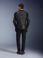 Jaqueta de Couro Alpinestars GP Plus R V4 Airflow, preta, vista traseira de piloto com equipamento completo, apresenta couro perfurado para ventilação e detalhes do logótipo em vermelho, design desportivo elegante, combinada com calças pretas e botas de motociclismo