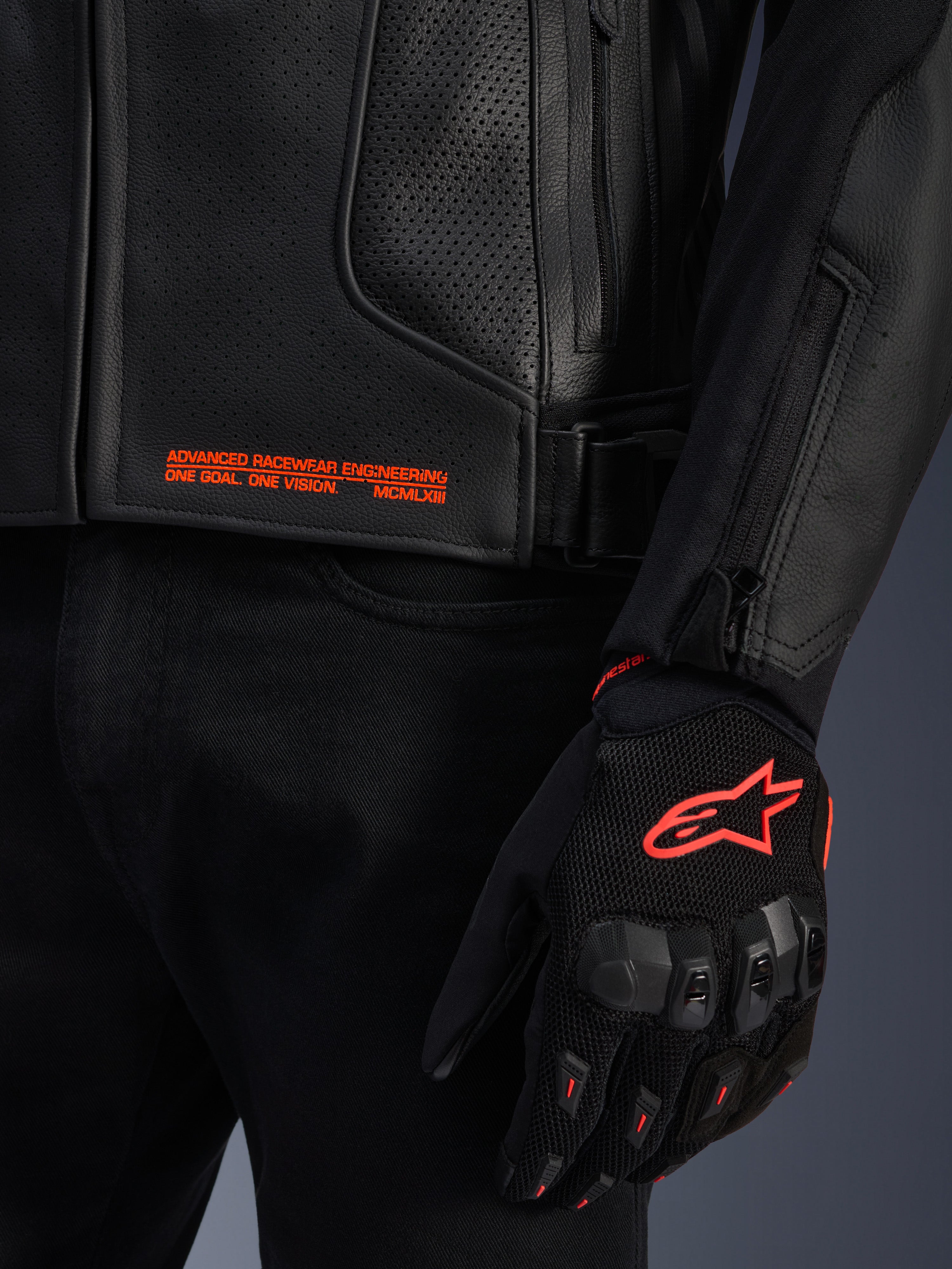 Alpinestars GP Plus R V4 Airflow Leather Jacket, grande plano de couro perfurado preto com texto gráfico cor-de-laranja, acompanhado por uma luva de motociclismo preta e cor-de-laranja com o logótipo Astars