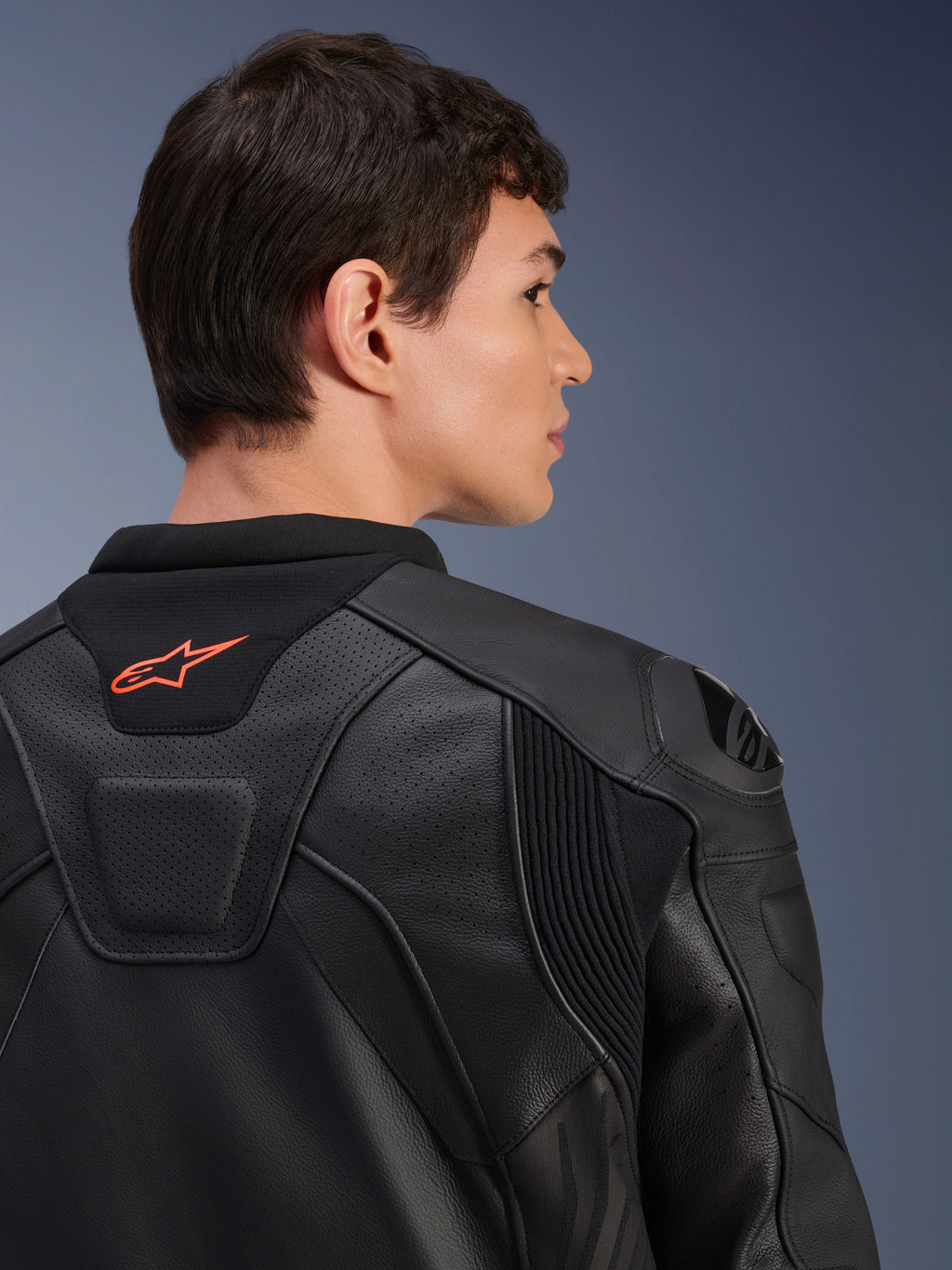 Jaqueta de Couro Alpinestars GP Plus R V4 Airflow, preta, vista traseira aproximada num modelo, com couro perfurado de grau de competição, painéis elásticos técnicos e pequeno logótipo Alpinestars cor de laranja na gola, vestuário profissional para motociclismo