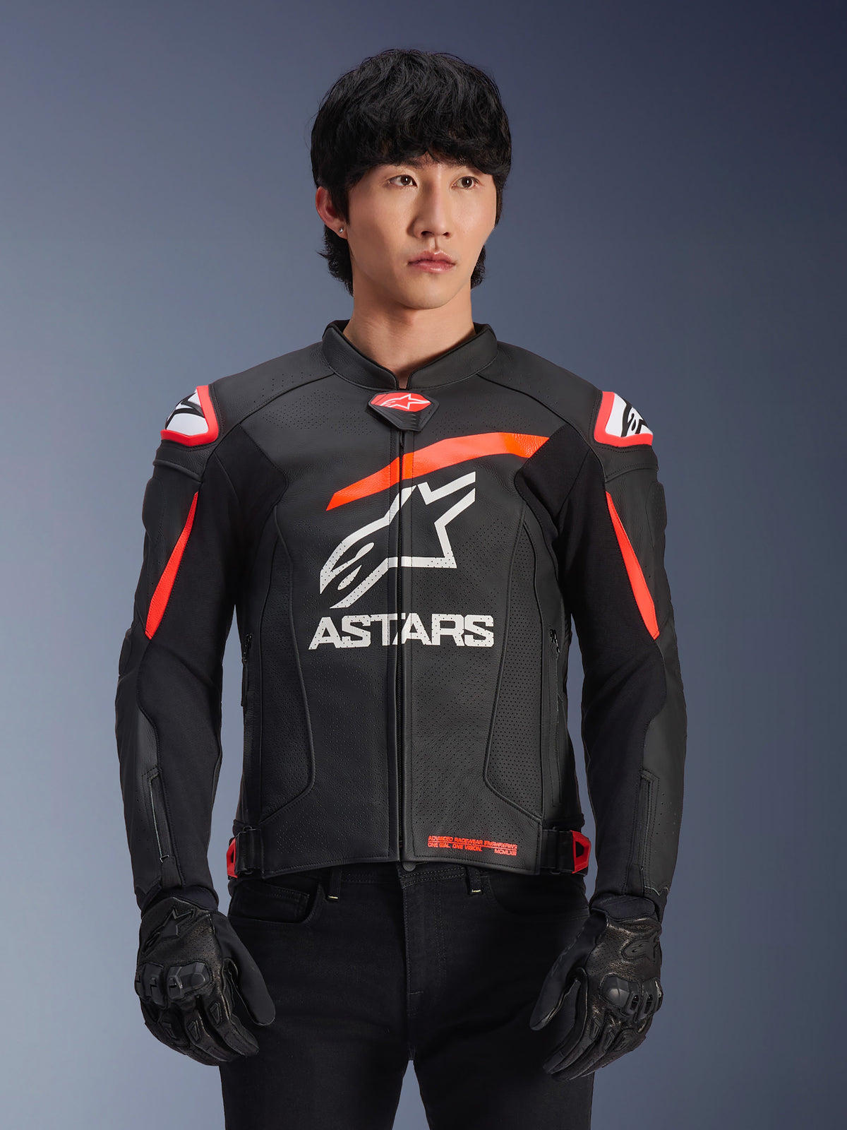 Casaco de pele Alpinestars GP Plus R V4 Airflow em preto com detalhes vermelho fluo e branco, vestido por um modelo, com construção em pele perfurada, um logótipo ASTARS branco de grandes dimensões no peito e proteção de ombro integrada para motociclismo de competição.