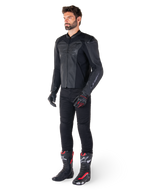 Man wearing Alpinestars Faster V3 Airflow Leather Jacket in Black Black, paired with black pants, black and red motorcycle gloves, and black racing boots with red and white accents, full-body sport riding gear