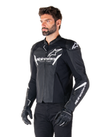 Alpinestars Faster V3 Airflow Leather Jacket, preto e branco, casaco de motociclismo desportivo com painéis de couro perfurado, logótipo Alpinestars branco no peito e braços, usado por um modelo com luvas e calças pretas, equipamento de condução elegante e protetor