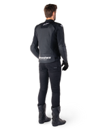 Casaco de couro Alpinestars Faster V3 Airflow, preto e branco, vista traseira com painéis de couro perfurado e marca Alpinestars proeminente na zona lombar, usado por um motociclista com calças, luvas e botas de condução pretas