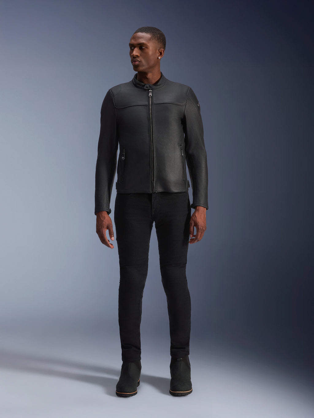 Male model wearing Alpinestars Blacktrack Leather Jacket, Black premium bovine leather, modern minimalist biker design with a tailored fit, paired with black riding pants and boots, urban contemporary style