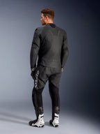 Casaco de Couro Alpinestars Caliber, casaco de motociclismo de estrada preto, vista traseira, com couro perfurado e inserções elásticas em acordeão na cintura e nos ombros, logótipo em relevo, usado com calças de couro pretas e botas de competição brancas.