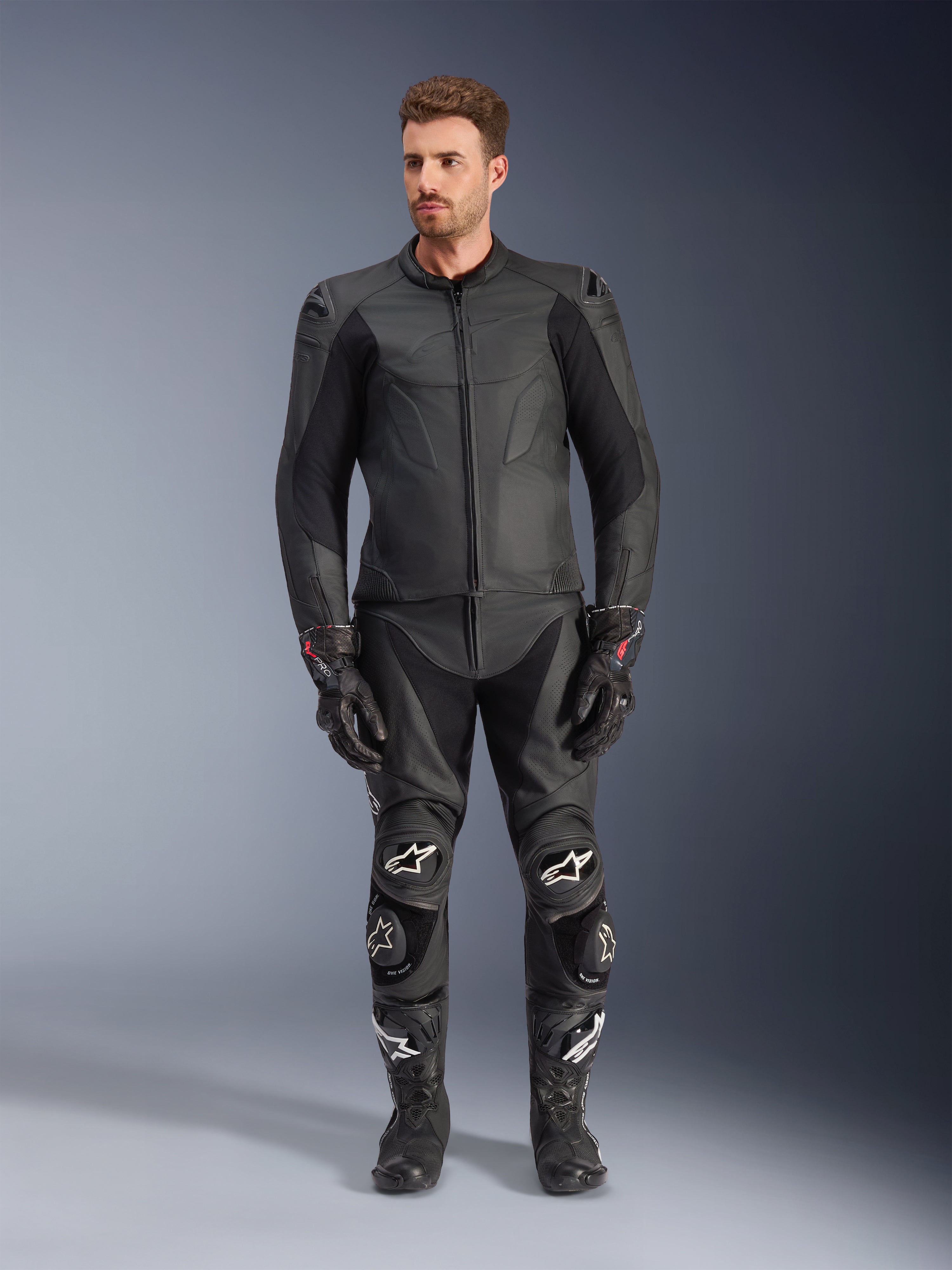 Casaco de Couro Alpinestars Caliber, casaco de motociclismo preto, usado com calças de corrida, luvas e botas a condizer, apresentando um design elegante com logótipos tonais, painéis elásticos nas mangas e sliders de proteção nos ombros, cenário de estúdio profissional