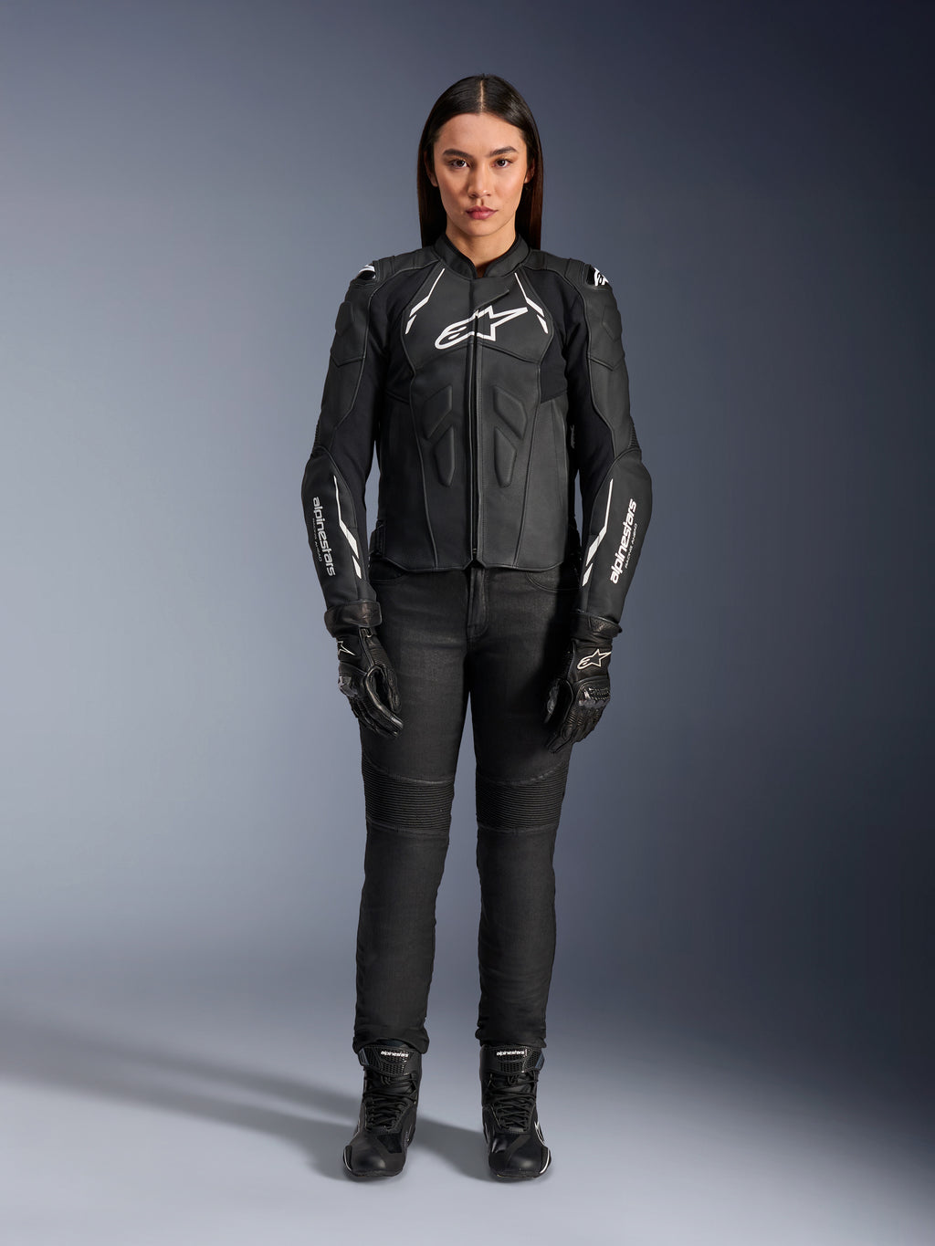 Alpinestars Woman Stella Dusk Leather Jacket, Black and White, worn by a model with matching black pants and boots, front view, featuring white Alpinestars logos on the chest and sleeves, premium bovine leather protective gear for women