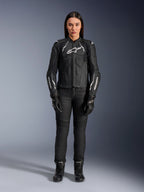 Alpinestars Woman Stella Dusk Leather Jacket, Black and White, worn by a model with matching black pants and boots, front view, featuring white Alpinestars logos on the chest and sleeves, premium bovine leather protective gear for women