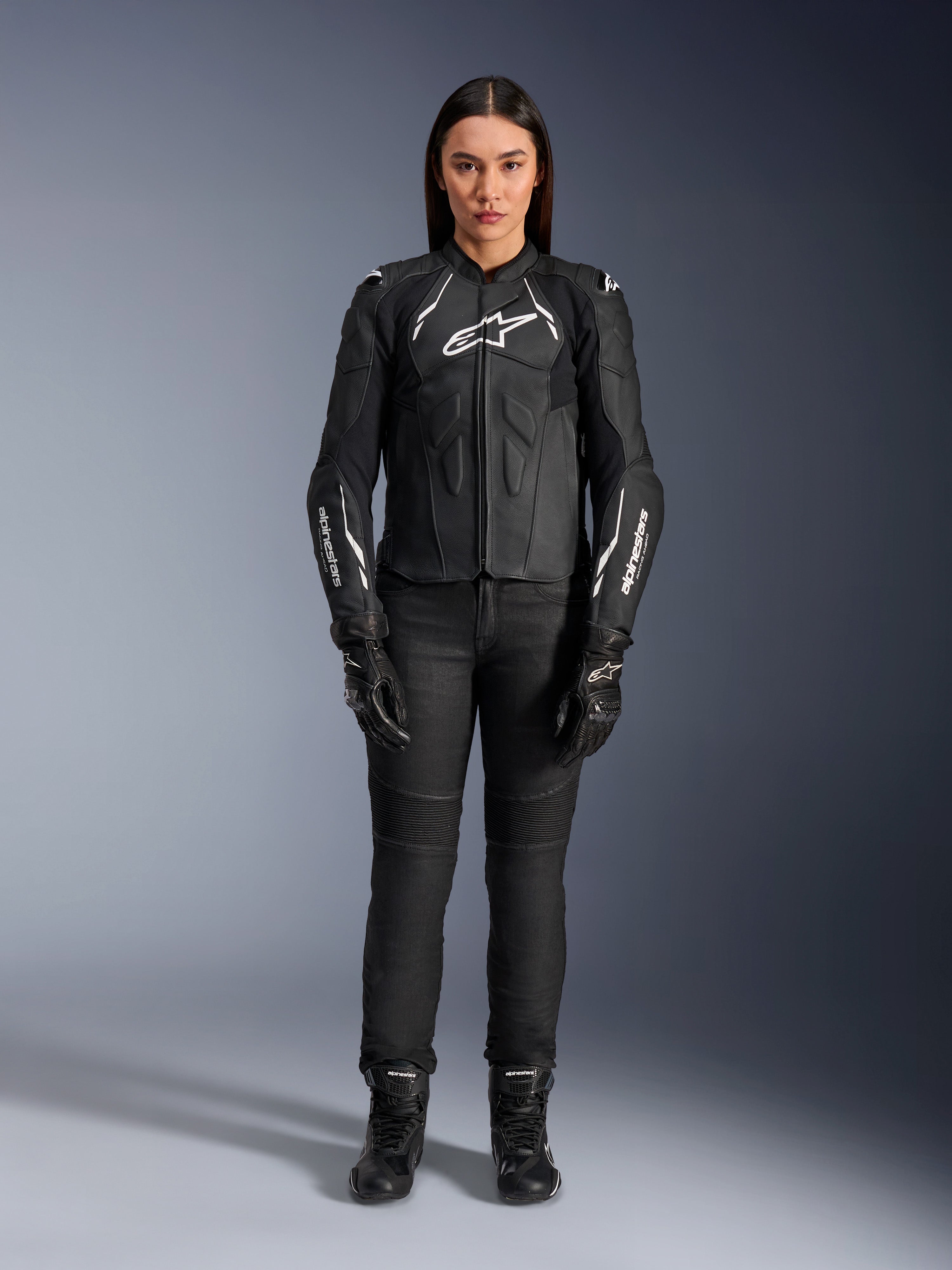 Alpinestars Woman Stella Dusk Leather Jacket, Black and White, worn by a model with matching black pants and boots, front view, featuring white Alpinestars logos on the chest and sleeves, premium bovine leather protective gear for women