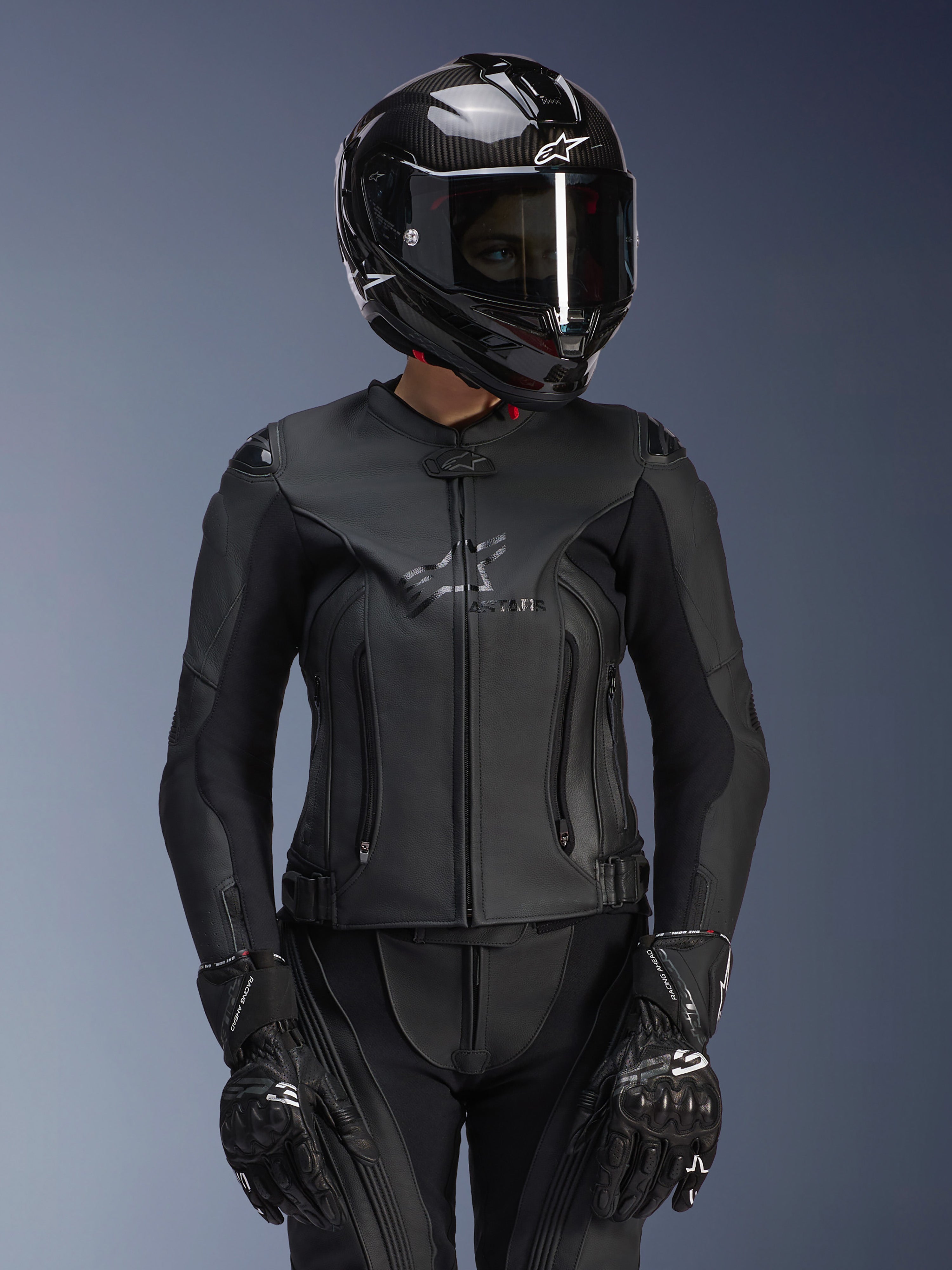 Alpinestars Women Stella GP Plus V4 Leather Jacket in Black Black, worn with a black carbon fiber helmet and racing gloves, sleek leather construction with subtle chest branding, tailored silhouette for female riders, professional sport motorcycle gear