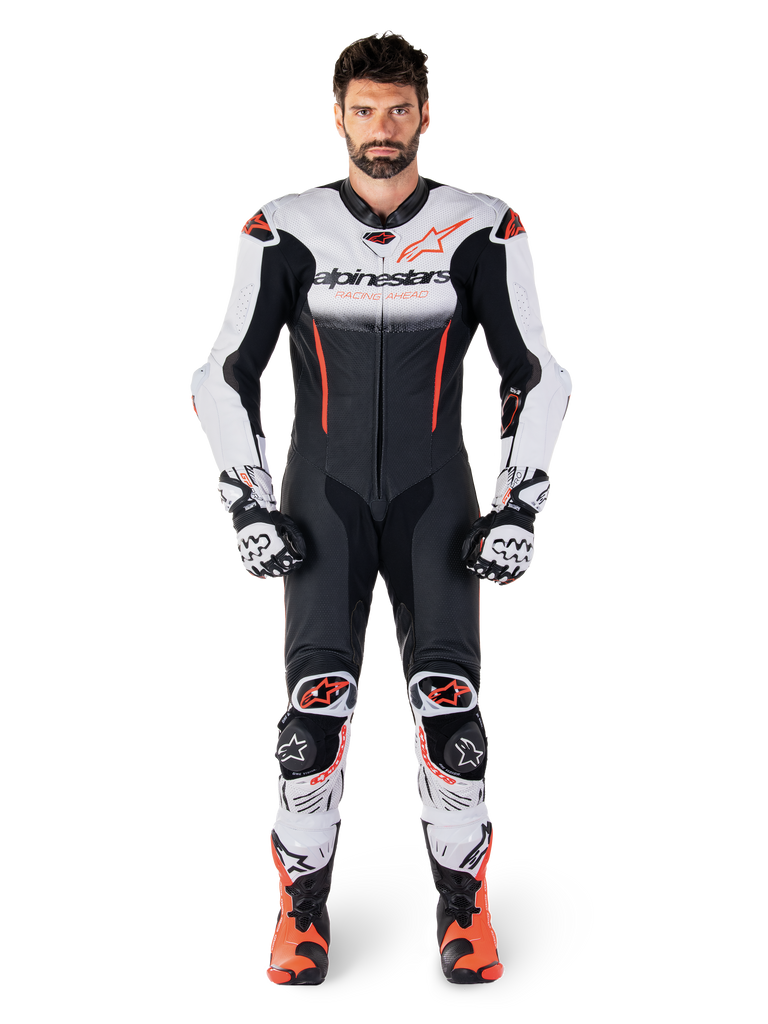 Piloto masculino a usar o fato de couro de uma peça Alpinestars GP-R7 em branco, preto e vermelho fluo, coordenado com luvas e botas de corrida a condizer, equipamento profissional de pista para motociclismo com um ajuste de corrida aerodinâmico e marca destacada
