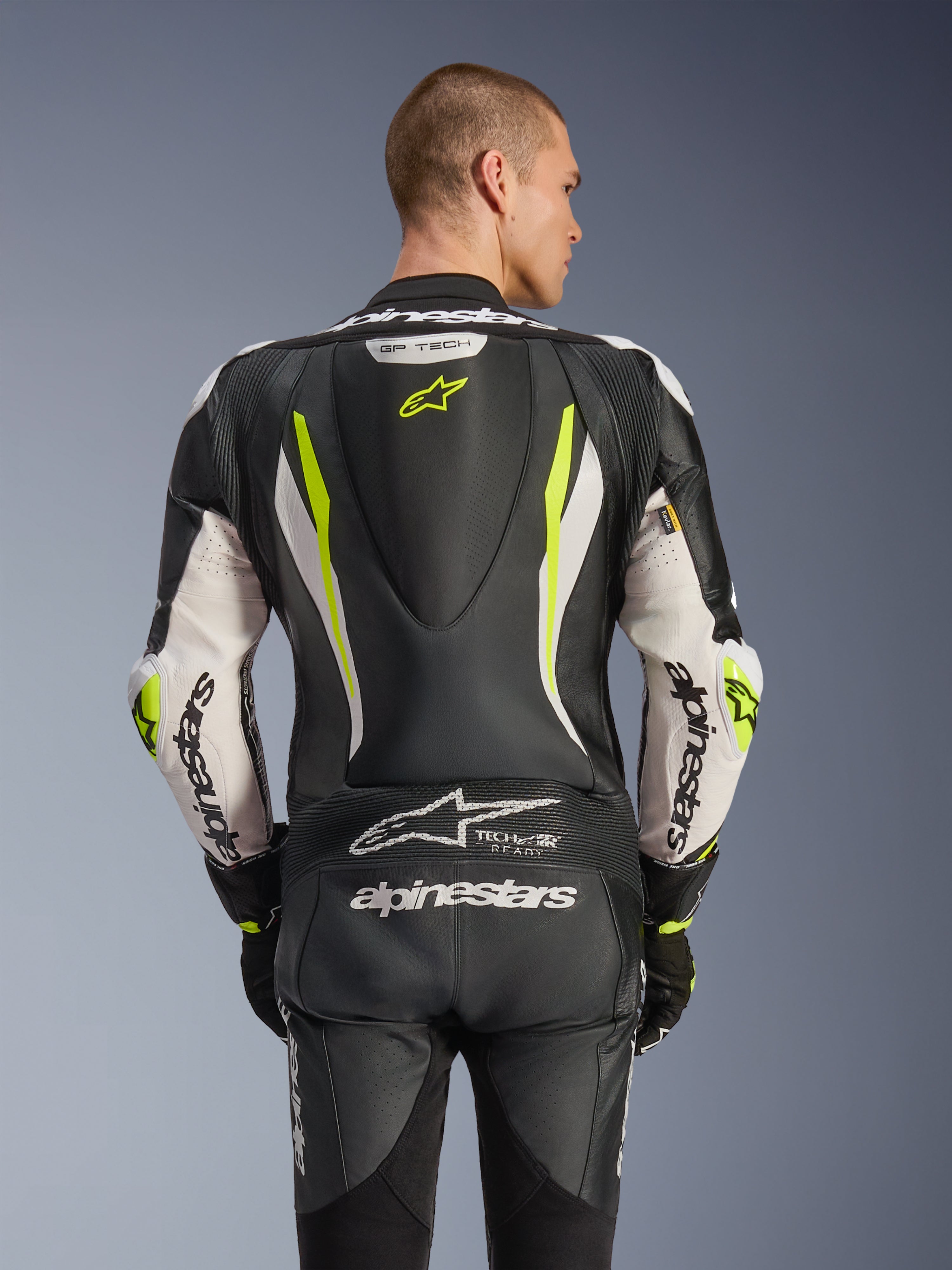 Alpinestars GP Tech V5 One Piece Leather Suit, back view on model, Black White and Yellow Fluo, featuring aerodynamic hump, large Alpinestars branding on arms and seat, accordion stretch panels, and Tech-Air Ready logo