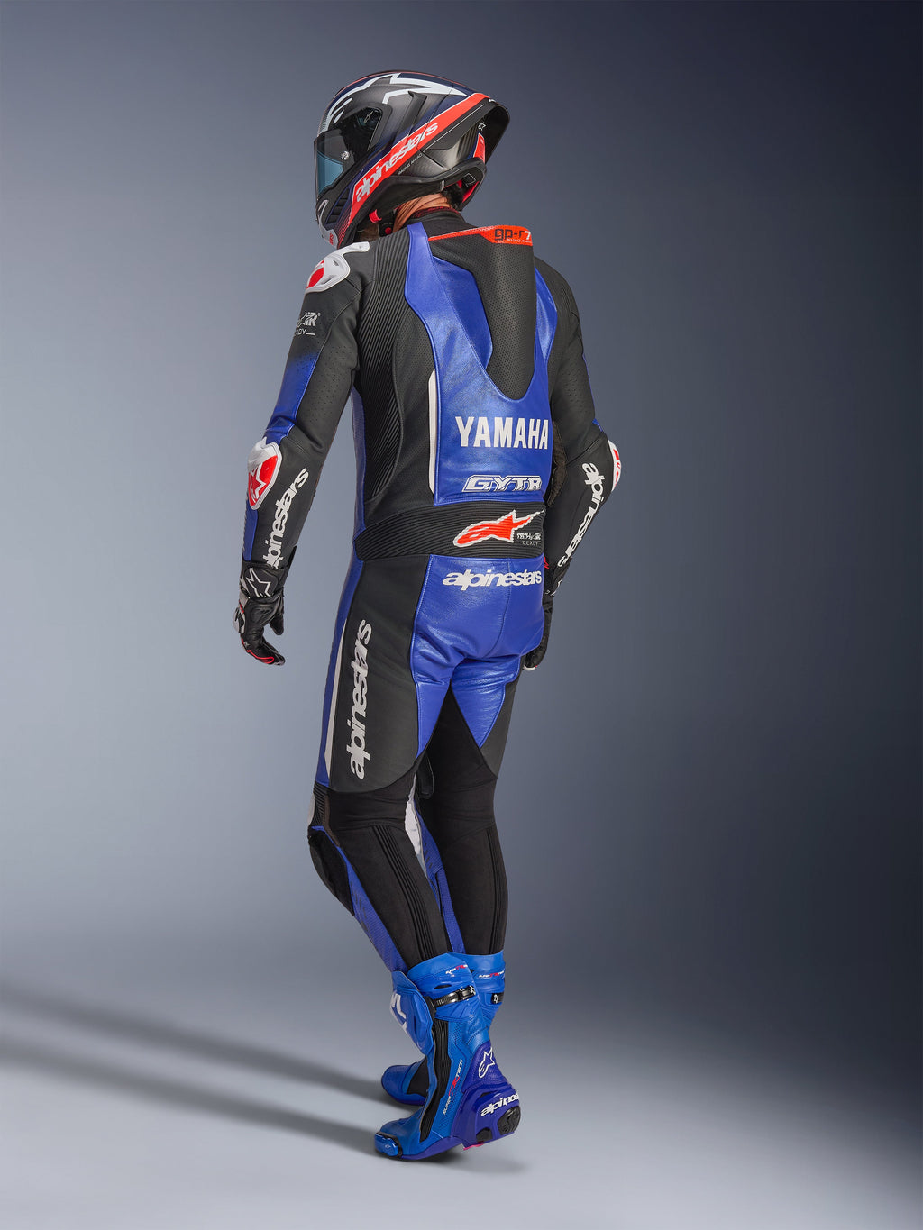 Fato de Couro Alpinestars Yamaha GP-R7 de Uma Peça, azul metálico, preto e branco, vista traseira com corcunda aerodinâmica e logótipo Yamaha, usado com botas de corrida e capacete azuis a condizer, fato de performance profissional para corridas em pista