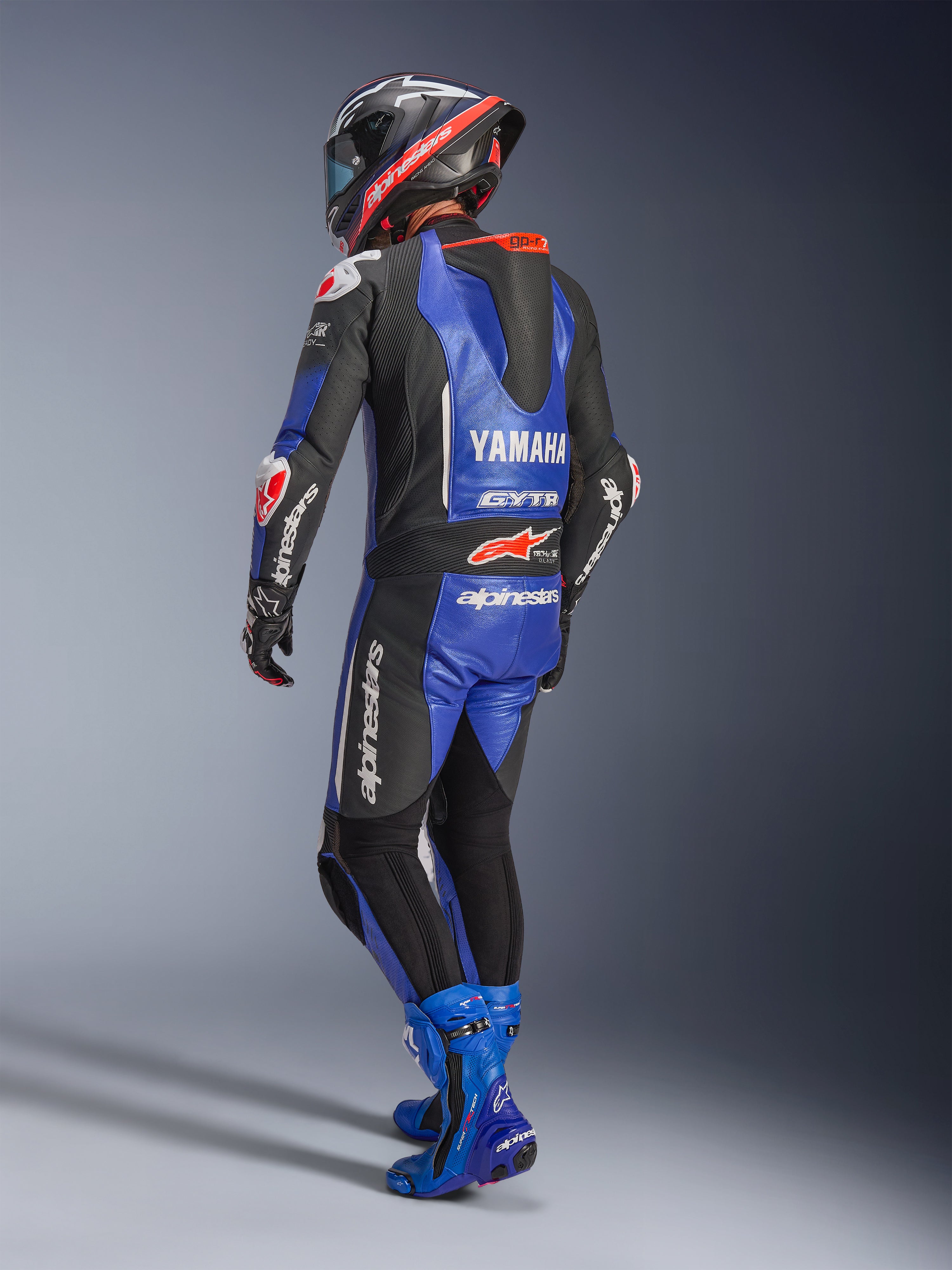 Fato de Couro Alpinestars Yamaha GP-R7 de Uma Peça, azul metálico, preto e branco, vista traseira com corcunda aerodinâmica e logótipo Yamaha, usado com botas de corrida e capacete azuis a condizer, fato de performance profissional para corridas em pista