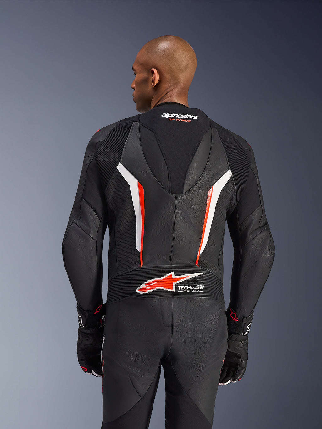 Alpinestars GP Force V2 Leather Suit, fato de motociclismo de 1 peça, preto, branco e vermelho fluo, vista traseira da parte superior do corpo mostrando a pele perfurada e o logótipo Tech-Air Ready, usado com luvas pretas e vermelhas a condizer