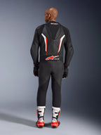 Vista traseira de um modelo a usar o Fato de Cabedal Alpinestars GP Force V2 de Uma Peça em Preto Branco Vermelho Fluo, destacando a corcova aerodinâmica e a marca Tech-Air Ready, combinado com botas de corrida profissionais brancas e vermelhas e luvas pretas.