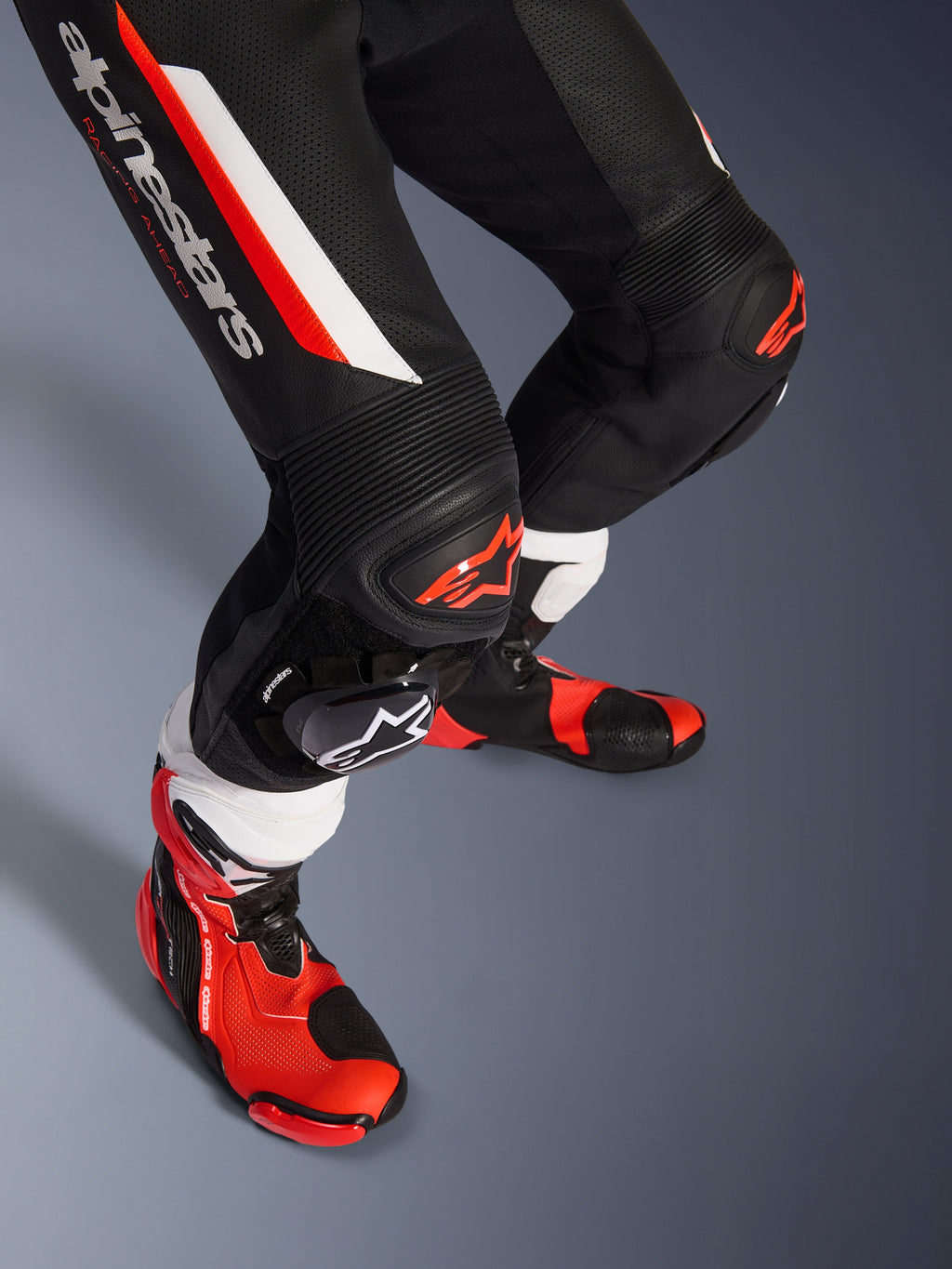 Alpinestars GP Force V2 1-Piece Leather Suit, preto, branco e vermelho fluorescente, grande plano da zona inferior das pernas e joelhos com protetores DFS Lite e sliders substituíveis, combinado com botas de corrida profissionais