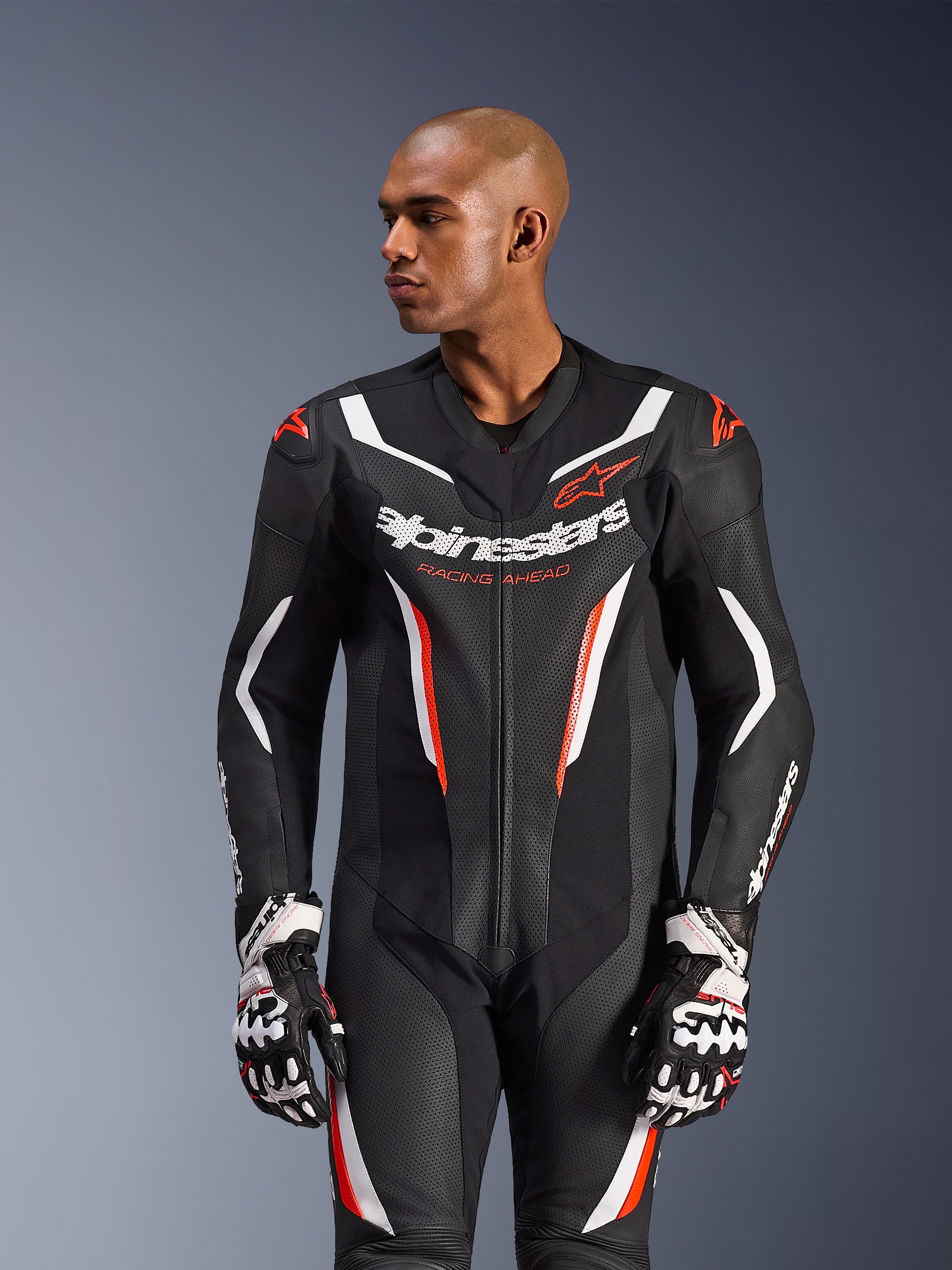 Fato de Cabedal Alpinestars GP Force V2 - 1 Peça, fato de motociclismo, preto, branco e vermelho fluo, com painéis de pele perfurada, logótipo de destaque no peito com o texto 'Racing Ahead' e design ergonómico de proteção, usado com luvas de competição a condizer
