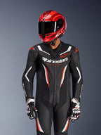 Motociclista a usar o fato de pele Alpinestars GP Force V2 de uma peça em preto, branco e vermelho fluo, capacete de corrida e luvas em vermelho coordenado, apresenta painéis de pele perfurada e logótipos em destaque, equipamento de corrida de alta performance