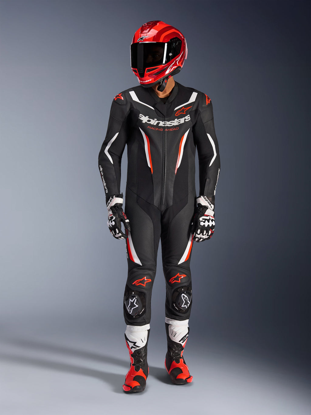 Fato de Pele Alpinestars GP Force V2 - 1 Peça, Preto, Branco e Vermelho Fluo, usado com um capacete de corrida vermelho, luvas pretas e brancas, e botas vermelhas e pretas, com painéis de pele perfurada e logótipos Alpinestars, equipamento profissional de corrida de motociclismo